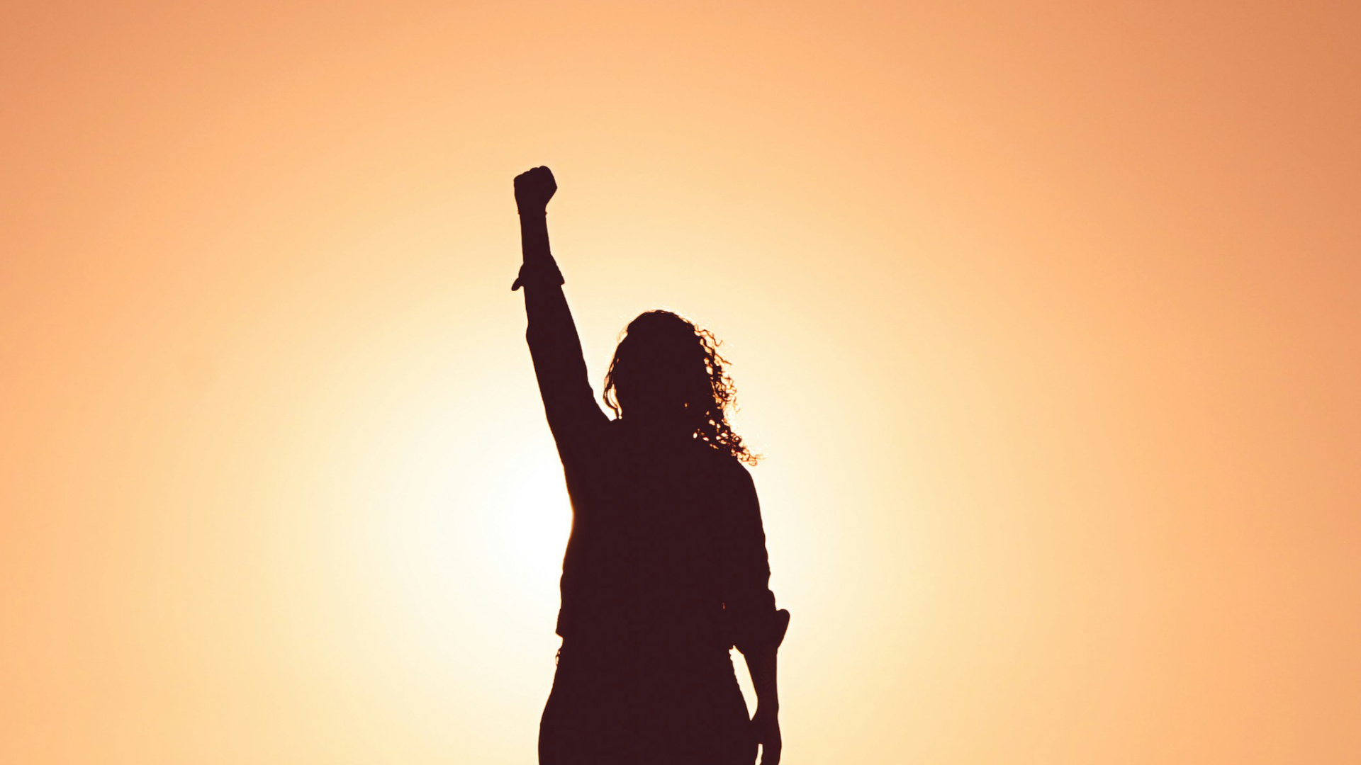 Mujer con el puño en alto al atardecer, simbolizando el empoderamiento y apoyo que se ofrecen en el Grupo de Supervisión.